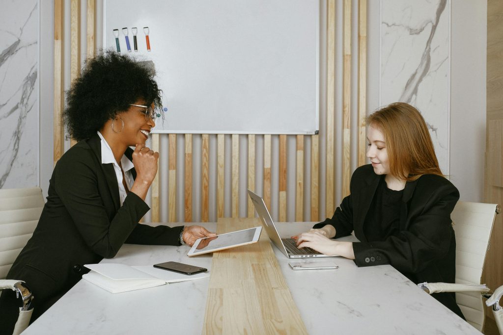 Two businesswomen engaged in a meeting discussing plans using digital devices in a modern office.